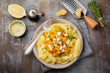 Fırında kabak, beyaz peynir ve baharat otlar gri beton eski arka plan üzerinde seramik plaka ile makarna Mafaldine Napoletane. Seçici odak. Rustik tarzı. Üstten Görünüm.