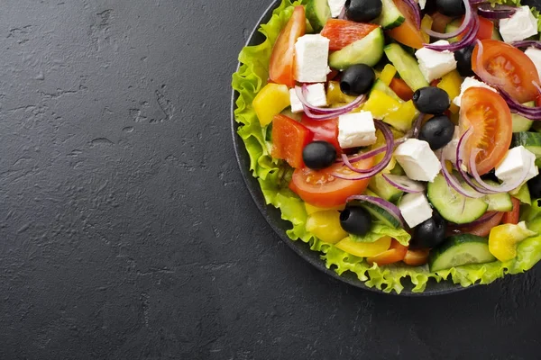 Yunan salatası siyah beton zemin üzerine seramik plaka. Geleneksel Yunan yemeği. Seçici odak. Üstten Görünüm.