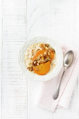 Karamelize Trabzon hurması ve ceviz Beyaz ahşap zemin üzerinde hafif bir seramik kase ile yulaf lapası. Seçici odak. Üstten Görünüm. Kopya alanı.