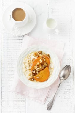 Karamelize Trabzon hurması ve ceviz Beyaz ahşap zemin üzerinde hafif bir seramik kase ile yulaf lapası. Seçici odak. Üstten Görünüm. Kopya alanı.