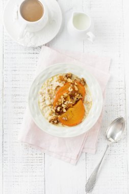 Karamelize Trabzon hurması ve ceviz Beyaz ahşap zemin üzerinde hafif bir seramik kase ile yulaf lapası. Seçici odak. Üstten Görünüm. Kopya alanı.