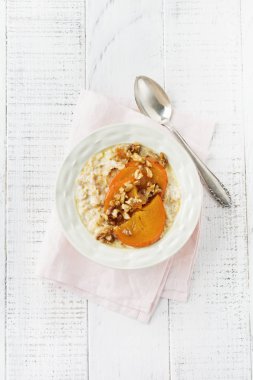 Karamelize Trabzon hurması ve ceviz Beyaz ahşap zemin üzerinde hafif bir seramik kase ile yulaf lapası. Seçici odak. Üstten Görünüm. Kopya alanı.