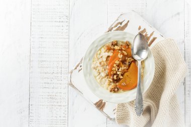 Karamelize Trabzon hurması ve ceviz Beyaz ahşap zemin üzerinde hafif bir seramik kase ile yulaf lapası. Seçici odak. Üstten Görünüm. Kopya alanı.