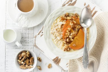 Karamelize Trabzon hurması ve ceviz Beyaz ahşap zemin üzerinde hafif bir seramik kase ile yulaf lapası. Seçici odak. Üstten Görünüm. Kopya alanı.