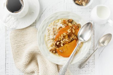 Karamelize Trabzon hurması ve ceviz Beyaz ahşap zemin üzerinde hafif bir seramik kase ile yulaf lapası. Seçici odak. Üstten Görünüm. Kopya alanı.