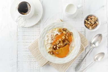 Karamelize Trabzon hurması ve ceviz Beyaz ahşap zemin üzerinde hafif bir seramik kase ile yulaf lapası. Seçici odak. Üstten Görünüm. Kopya alanı.