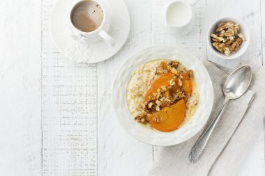 Karamelize Trabzon hurması ve ceviz Beyaz ahşap zemin üzerinde hafif bir seramik kase ile yulaf lapası. Seçici odak. Üstten Görünüm. Kopya alanı.