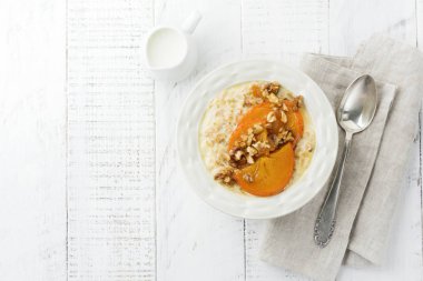 Karamelize Trabzon hurması ve ceviz Beyaz ahşap zemin üzerinde hafif bir seramik kase ile yulaf lapası. Seçici odak. Üstten Görünüm. Kopya alanı.