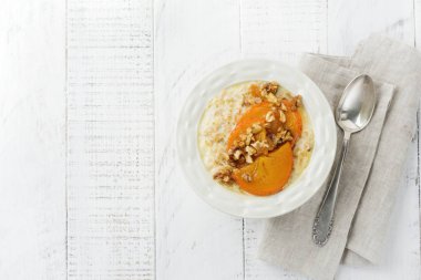 Karamelize Trabzon hurması ve ceviz Beyaz ahşap zemin üzerinde hafif bir seramik kase ile yulaf lapası. Seçici odak. Üstten Görünüm. Kopya alanı.