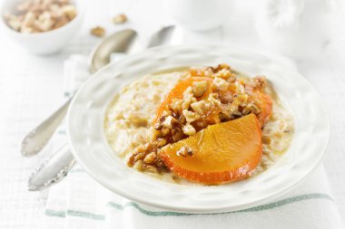 Karamelize Trabzon hurması ve ceviz Beyaz ahşap zemin üzerinde hafif bir seramik kase ile yulaf lapası. Seçici odak. Üstten Görünüm. Kopya alanı.