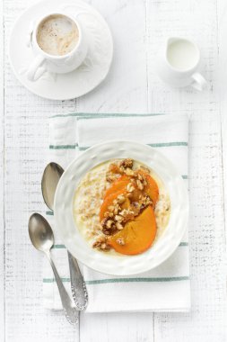 Karamelize Trabzon hurması ve ceviz Beyaz ahşap zemin üzerinde hafif bir seramik kase ile yulaf lapası. Seçici odak. Üstten Görünüm. Kopya alanı.