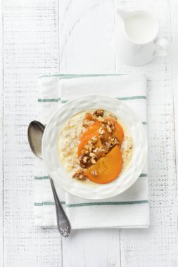 Karamelize Trabzon hurması ve ceviz Beyaz ahşap zemin üzerinde hafif bir seramik kase ile yulaf lapası. Seçici odak. Üstten Görünüm. Kopya alanı.