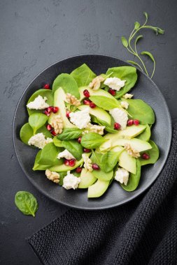 Taze yararlı vejetaryen sağlıklı avokado, ıspanak, nar taneleri, ceviz, safran, biber ve ricotta Salata siyah arka plan üzerine. Seçici odak. Üstten Görünüm. Metin için yer kopyalayın.