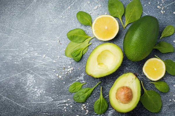 Raw fresh avocado, spinach leaves and lemon on dark old concrete or stone background. Selective focus. Top view. Copy space.