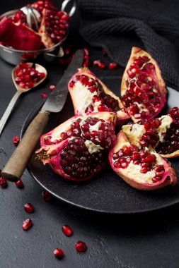 Taze olgun nar, siyah beton veya taş arka plan üzerinde parçalar halinde kesilmiş. Seçici odak. Metin için yer. 