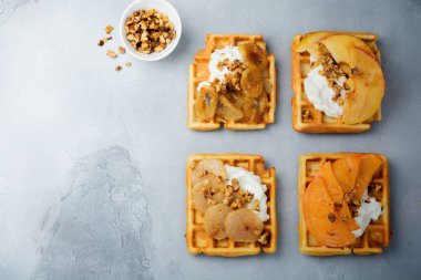 Karamelize meyve, elma, muz, Trabzon hurması, armut ve gri beton veya taş zemin üzerine ceviz ile lezzetli Belçika doldurmuştu. Kahvaltı için fikirler. Seçici odak. Üstten Görünüm. Metin için yer.