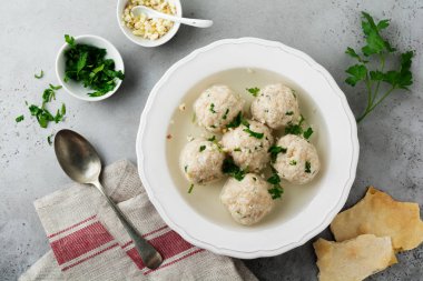 Maydanoz ve sarımsak bir gri taş veya beton arka plan basit beyaz seramik plaka ile ev yapımı tavuk matzo topu çorbası. Geleneksel Yahudi Fısıh çanağı. Seçici odak. Üstten Görünüm.