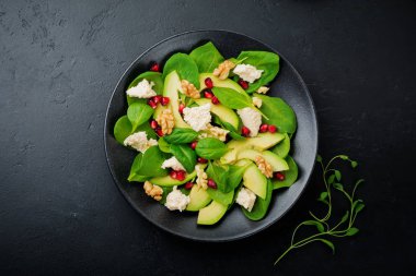 Taze yararlı vejetaryen sağlıklı avokado, ıspanak, nar taneleri, ceviz, safran, biber ve ricotta Salata siyah arka plan üzerine. Seçici odak. Üstten Görünüm. Metin için yer kopyalayın.