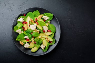 Taze yararlı vejetaryen sağlıklı avokado, ıspanak, nar taneleri, ceviz, safran, biber ve ricotta Salata siyah arka plan üzerine. Seçici odak. Üstten Görünüm. Metin için yer kopyalayın.