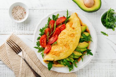 Avokado, domates ve roka ışık taş zemin üzerine beyaz seramik plaka üzerinde omlet. Sağlıklı kahvaltı. Seçici odak. Üstten Görünüm. Kopya alanı.