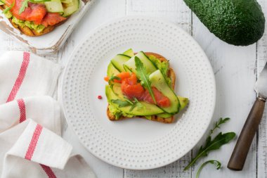 Alabalık, somon, avokado, salatalık ve roka ahşap stand Beyaz ahşap masa arka plan üzerine açık tost. Seçici odak. Üstten Görünüm. Kopya alanı