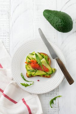 Alabalık, somon, avokado, salatalık ve roka ahşap stand Beyaz ahşap masa arka plan üzerine açık tost. Seçici odak. Üstten Görünüm. Kopya alanı