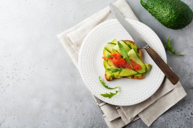 Alabalık, somon, avokado, salatalık ve roka ahşap stand gri beton zemin üzerine açık tost. Seçici odak. Üstten Görünüm. Kopya alanı