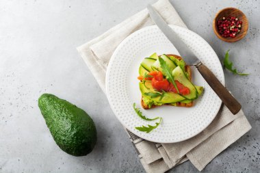 Alabalık, somon, avokado, salatalık ve roka ahşap stand gri beton zemin üzerine açık tost. Seçici odak. Üstten Görünüm. Kopya alanı