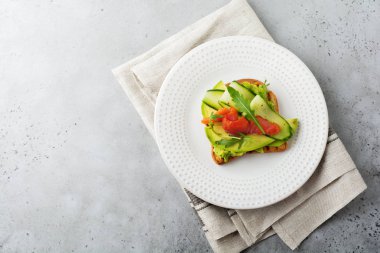 Alabalık, somon, avokado, salatalık ve roka ahşap stand gri beton zemin üzerine açık tost. Seçici odak. Üstten Görünüm. Kopya alanı