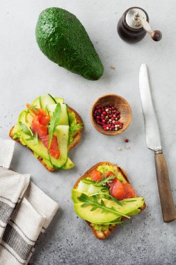 Alabalık, somon, avokado, salatalık ve roka ahşap stand gri beton zemin üzerine açık tost. Seçici odak. Üstten Görünüm. Kopya alanı