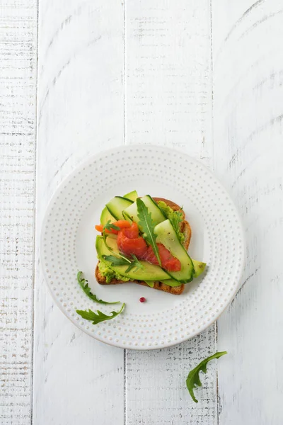 Alabalık, somon, avokado, salatalık ve roka ahşap stand Beyaz ahşap masa arka plan üzerine açık tost. Seçici odak. Üstten Görünüm. Kopya alanı