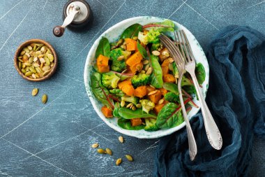 Fırında kabak, pazı, brokoli ve kabak çekirdeği seramik plaka taş veya beton arka plan tablo arka plan salatası. Seçici odak. Rustik tarzı. Üstten Görünüm. Kopya alanı.