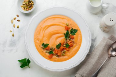 Eski bir taş veya beton zemin üzerine beyaz seramik tabak içinde ev yapımı balkabağı çorbası. Seçici odak. Üstten Görünüm. Kopya alanı.