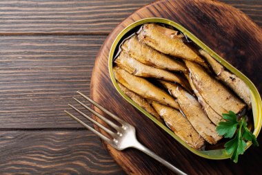 Koyu kahverengi zemin üzerine çatal ile teneke kutuda hamsi konserve. Seçici odak. Rustik tarzı. Üstten Görünüm. Kopya alanı.