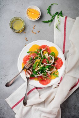 Narenciye vitamini salata. Portakal, greyfurt, ricotta peyniri, çam fıstığı, kırmızı soğan ve seramik plaka gri beton veya taş eski arka plan üzerinde Zeytinyağlı roka. Seçici odak. Üstten Görünüm. Kopya alanı.