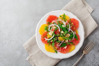 Narenciye vitamini salata. Portakal, greyfurt, ricotta peyniri, çam fıstığı, kırmızı soğan ve seramik plaka gri beton veya taş eski arka plan üzerinde Zeytinyağlı roka. Seçici odak. Üstten Görünüm. Kopya alanı.