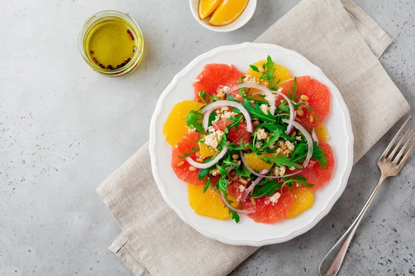 Narenciye vitamini salata. Portakal, greyfurt, ricotta peyniri, çam fıstığı, kırmızı soğan ve seramik plaka gri beton veya taş eski arka plan üzerinde Zeytinyağlı roka. Seçici odak. Üstten Görünüm. Kopya alanı.
