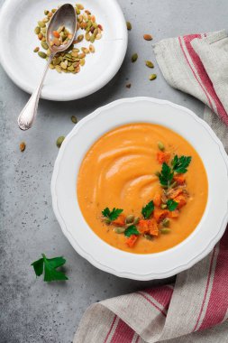 Eski gri beton veya taş zemin üzerine beyaz seramik tabak içinde ev yapımı balkabağı çorbası. Seçici odak. Üstten Görünüm. Kopya alanı.