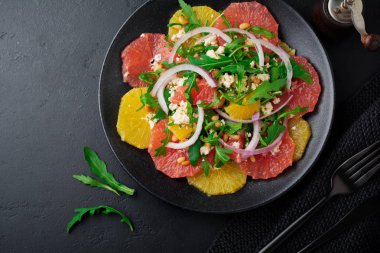 Narenciye vitamini salata. Portakal, greyfurt, ricotta peyniri, çam fıstığı, kırmızı soğan ve siyah beton veya taş eski arka plan üzerine seramik plaka Zeytinyağlı roka. Seçici odak. Üstten Görünüm. Kopya alanı.