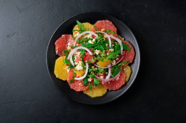 Narenciye vitamini salata. Portakal, greyfurt, ricotta peyniri, çam fıstığı, kırmızı soğan ve siyah beton veya taş eski arka plan üzerine seramik plaka Zeytinyağlı roka. Seçici odak. Üstten Görünüm. Kopya alanı.