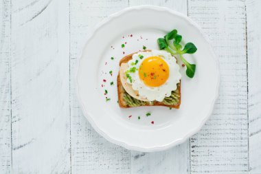 Avokado, peynir, kızarmış yumurta ve hafif ahşap arka plan üzerinde beyaz seramik tabak taze guacamole soslu kızarmış ekmek. Seçici odak. Üstten Görünüm.