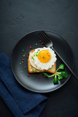 Avokado, peynir, kızarmış yumurta ve karanlık beton zemin üzerine siyah seramik tabak taze guacamole soslu kızarmış ekmek. Seçici odak. Üstten Görünüm.