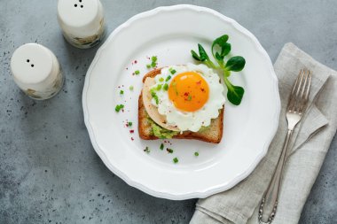 Avokado, peynir, kızarmış yumurta ve gri beton zemin üzerine beyaz seramik tabak taze guacamole soslu kızarmış ekmek. Seçici odak. Üstten Görünüm.