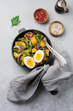 Sıcak patates salatası yeşil fasulye, biber, maydanoz, yumurta ve tavada gri beton zemin üzerine kırmızı soğan ile. Seçici odak. Üstten Görünüm. Kopya alanı.