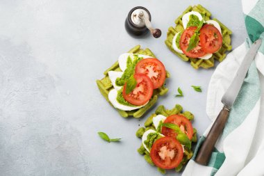 Ispanak ve mozzarella peyniri, pesto sos, domates ve fesleğen gri beton eski arka plan üzerinde yeşil gofret üzerinde sandviç. Seçici odak. Üstten Görünüm.