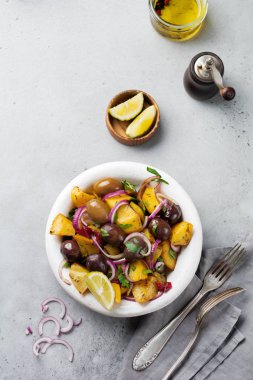 Zeytin, biber, maydanoz ve eski beyaz seramik plaka gri beton zemin üzerine kırmızı soğan ile sıcak patates salatası. Seçici odak. Üstten Görünüm. Kopya alanı.