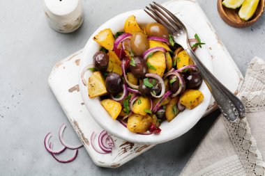Zeytin, biber, maydanoz ve eski beyaz seramik plaka gri beton zemin üzerine kırmızı soğan ile sıcak patates salatası. Seçici odak. Üstten Görünüm. Kopya alanı.