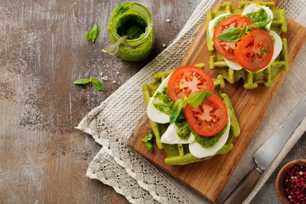 Ispanak ve mozzarella peyniri, pesto sos, domates ve fesleğen gri beton eski arka plan üzerinde yeşil gofret üzerinde sandviç. Seçici odak. Üstten Görünüm.