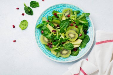 Ispanak bebek salata yaprakları, su teresi, kivi, avokado ve nar beyaz ışık ahşap zemin üzerinde mavi seramik tabak içinde. Seçici odak. Üstten Görünüm. Kopya alanı.