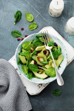 Ispanak bebek salata yaprakları, su teresi, kivi, avokado ve yaşlı seramik plaka gri beton zemin üzerine nar. Seçici odak. Üstten Görünüm. Kopya alanı.